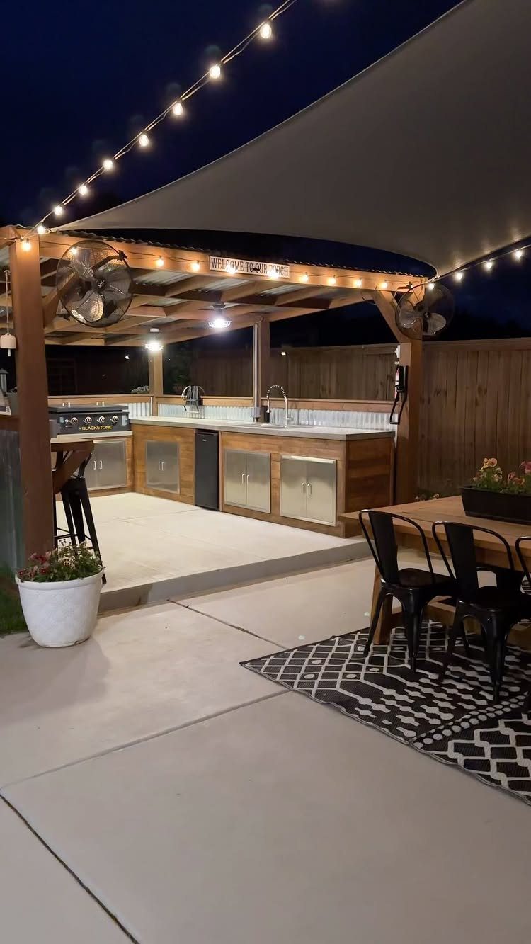 A wooden outdoor kitchen station with a built-in grill and sink under string lights.