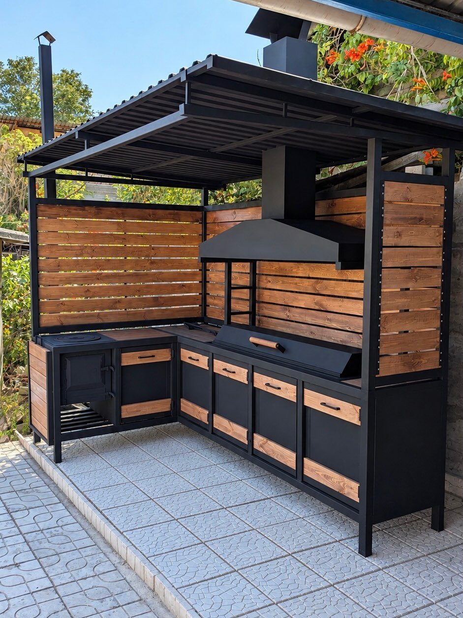 Black metal outdoor grilling station with wooden cabinets and drawers on a tiled patio.