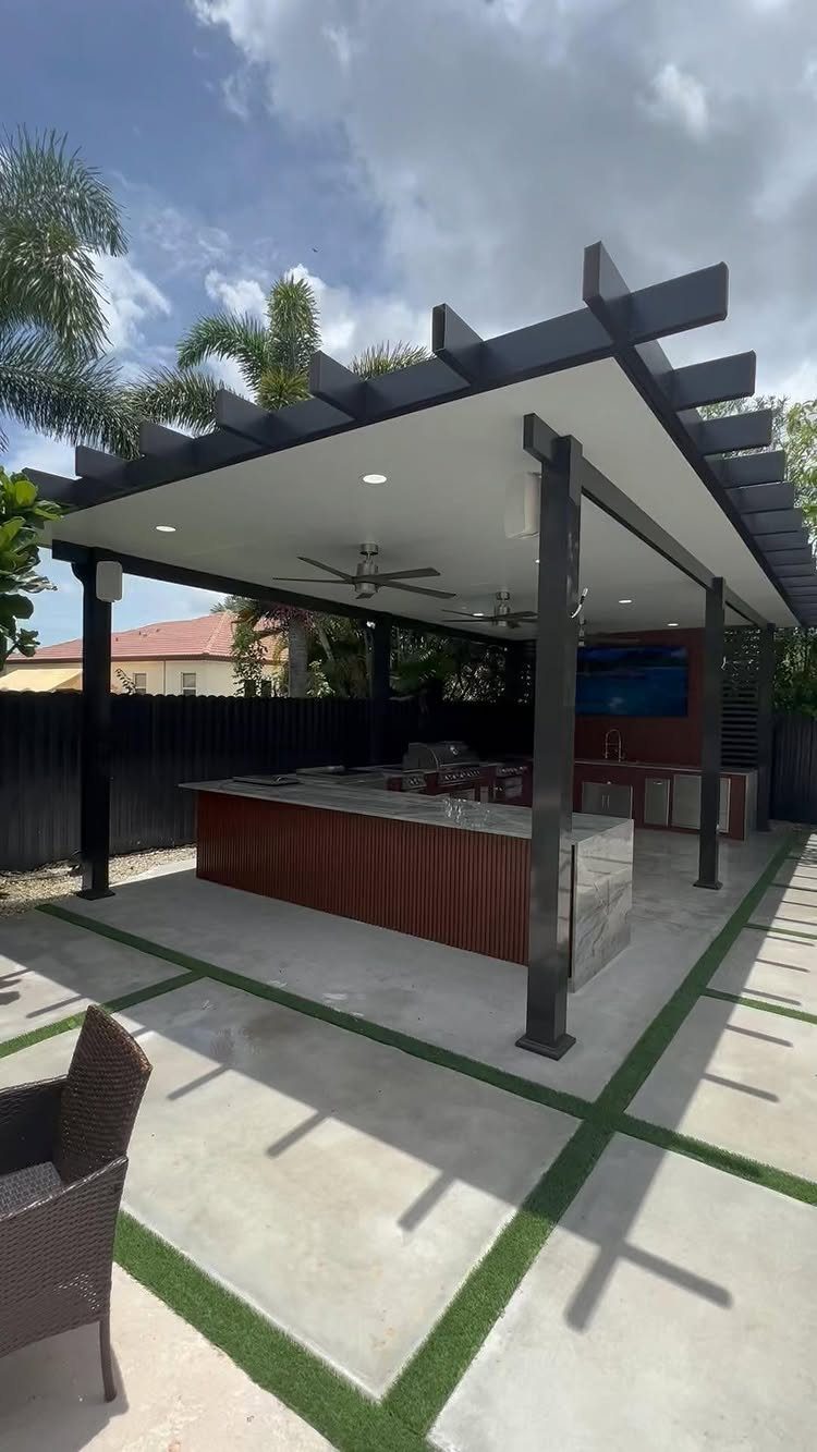 A modern outdoor kitchen station situated under a large black pergola with ceiling fans.