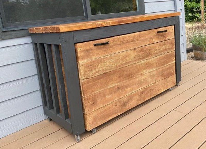 A compact wooden mobile grill station with a butcher block top on a deck.