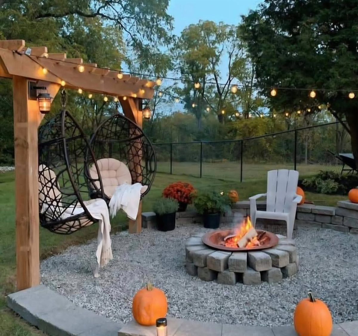 Hanging egg chairs and a fire pit arranged on a gravel patio under string lights.