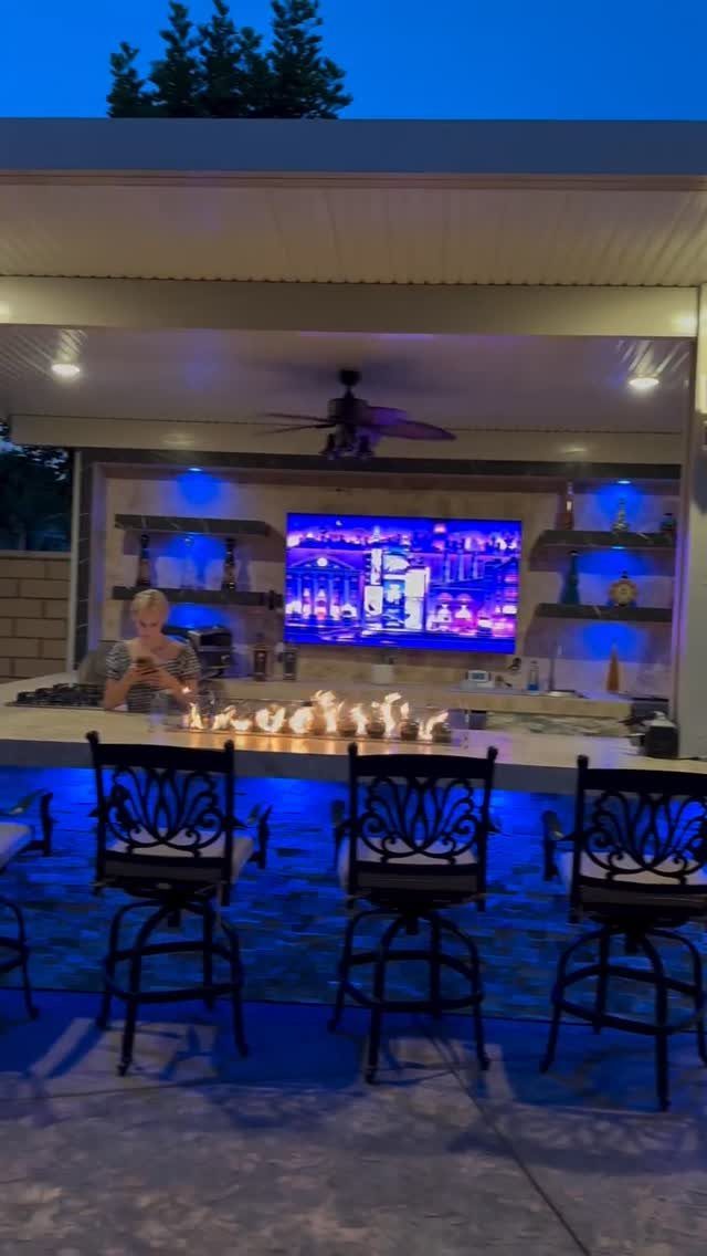 Outdoor bar area with blue lighting, bar stools, and a television under a covered patio.