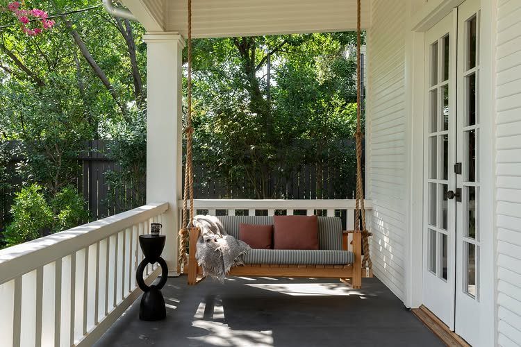 A wooden porch swing with striped cushions and a fur throw hanging on a white porch.