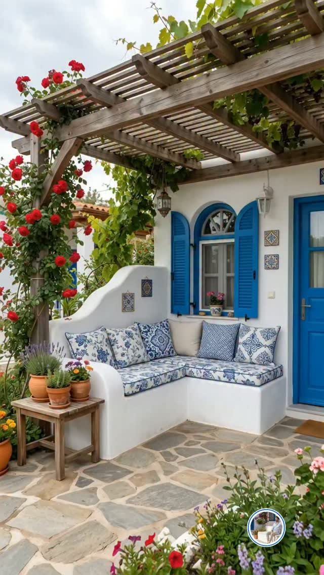 Built-in white corner bench with blue patterned cushions under a wooden pergola with climbing red roses.