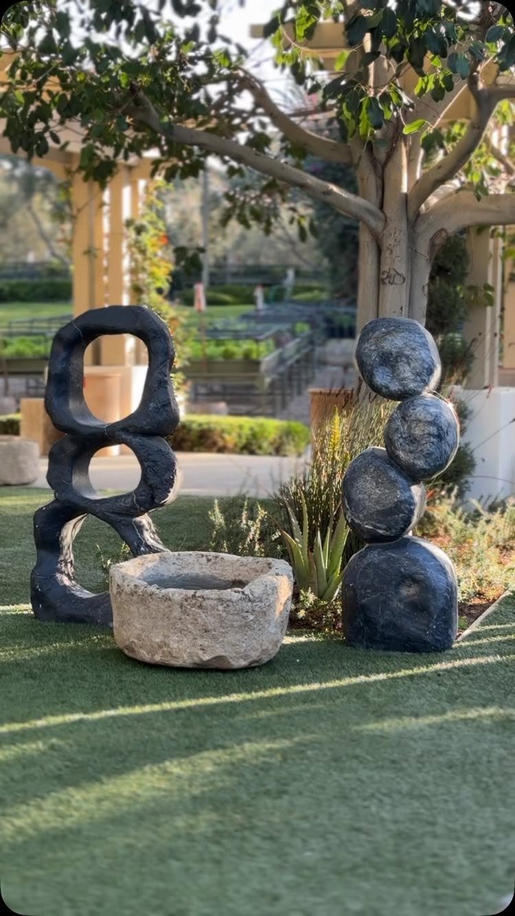 Abstract dark sculptures and a stone basin resting on green artificial turf outdoors.
