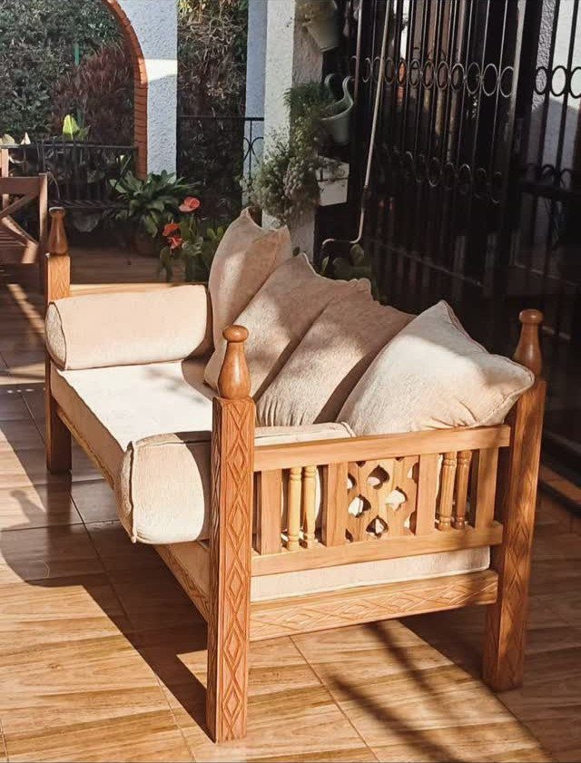 Wooden outdoor daybed with beige cushions and pillows on a tiled patio.