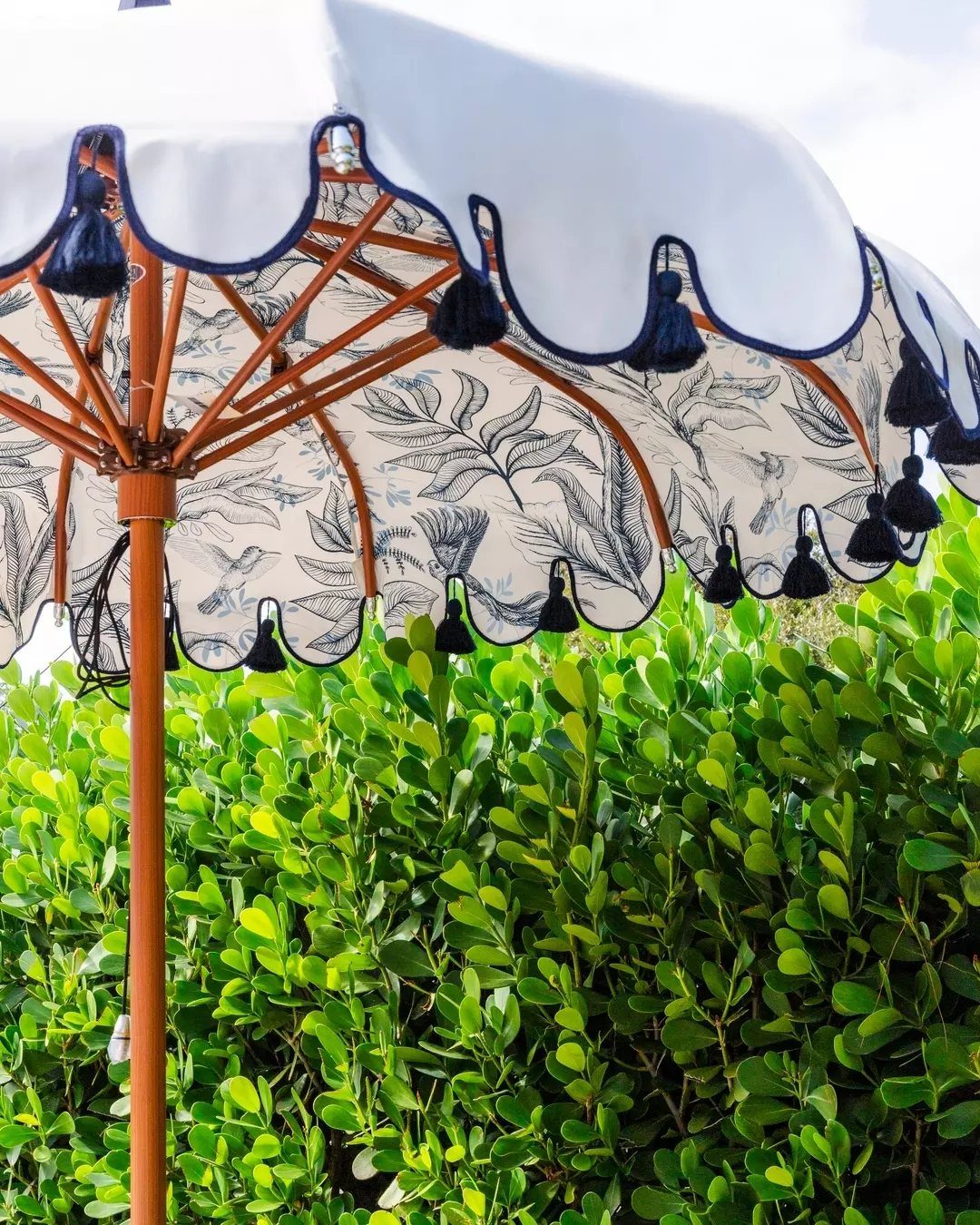 A decorative white patio umbrella with navy blue scalloped edges and hanging tassels.