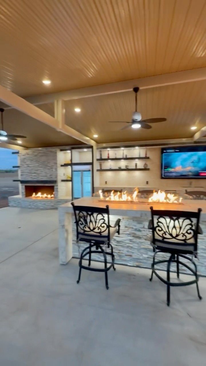 Stone outdoor kitchen bar with built-in fire feature and two black ornate bar stools.