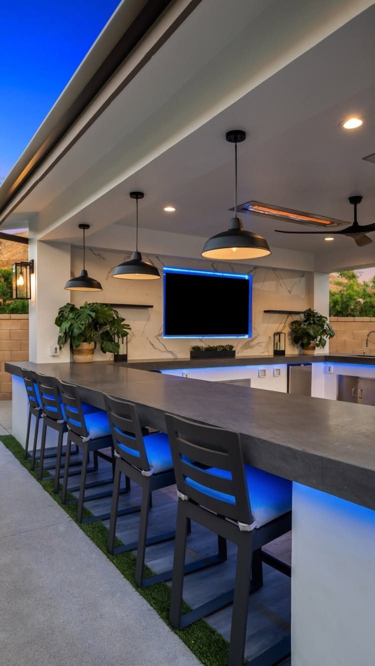 Modern outdoor bar with blue LED lighting, black pendant lights, and dark countertops under a covered patio.