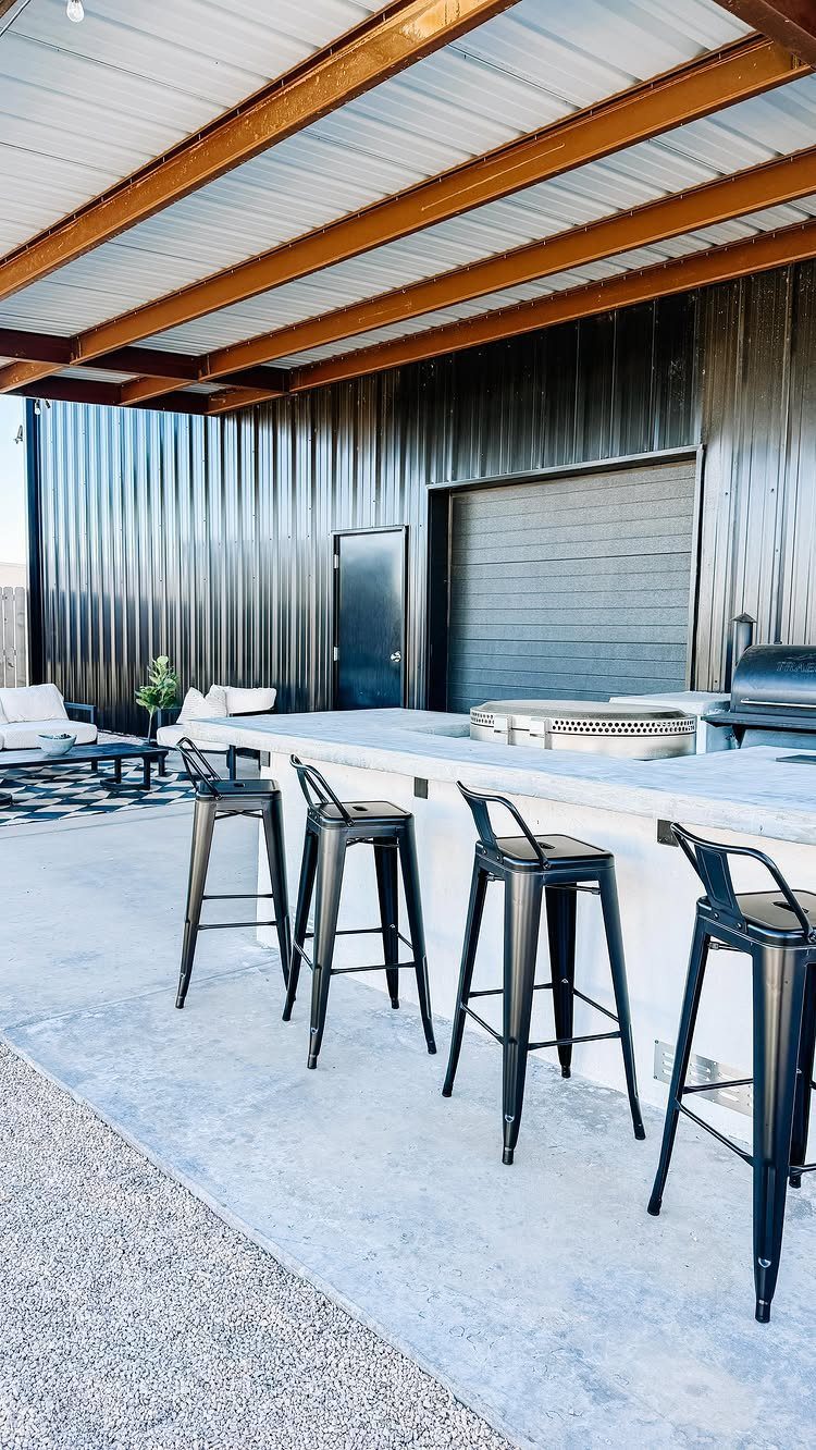 Four black metal bar stools lined up against a white outdoor kitchen counter.