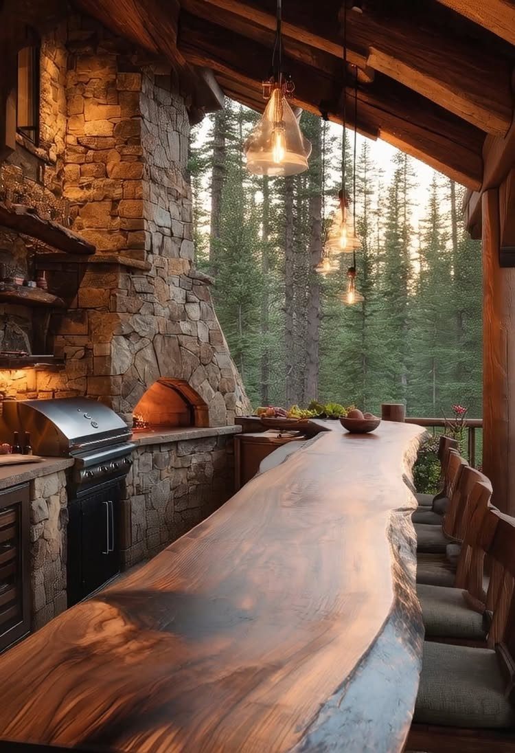 Rustic outdoor kitchen with stone walls and live-edge wood counter overlooking a pine forest.