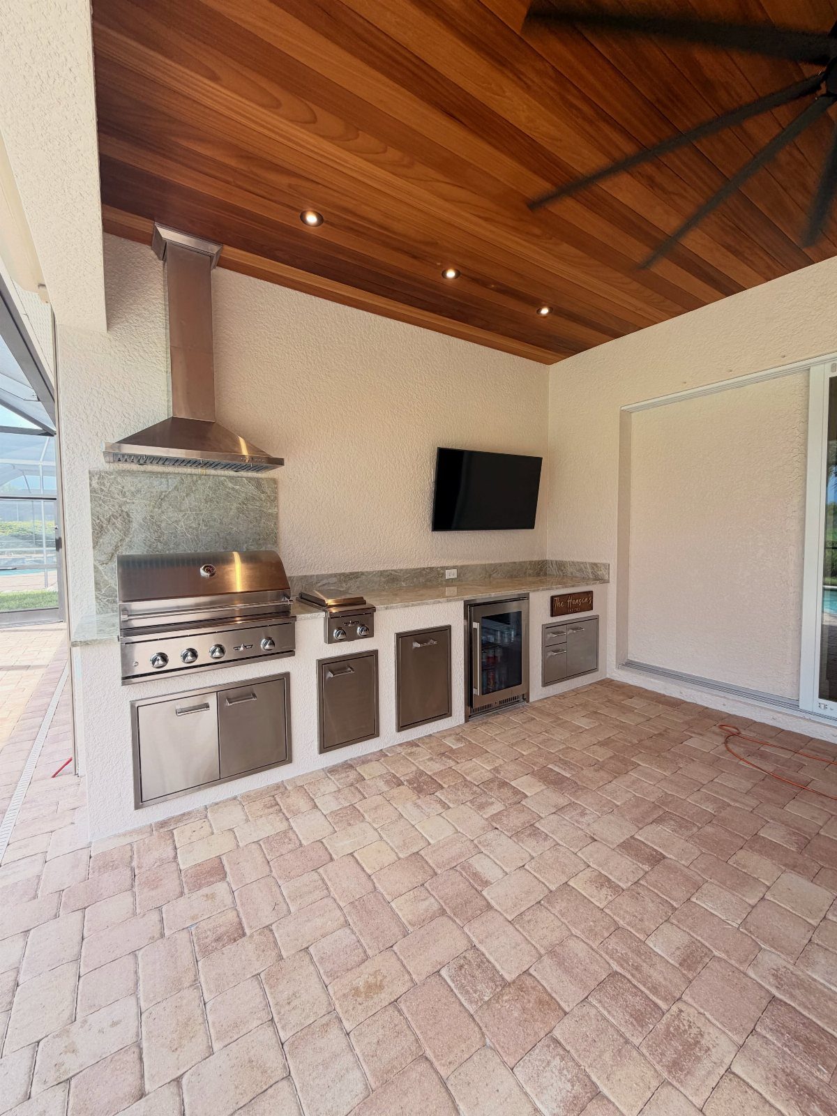 Stainless steel outdoor kitchen appliances installed under a stone countertop with a wood ceiling.