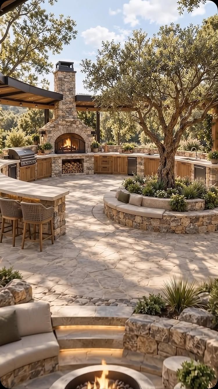 Stone outdoor kitchen with a large fireplace, built-in grill, and circular stone seating areas around a tree.