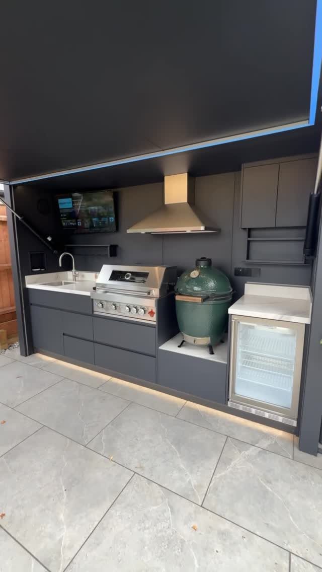 Modern dark grey outdoor kitchen featuring a stainless steel grill and green ceramic smoker.