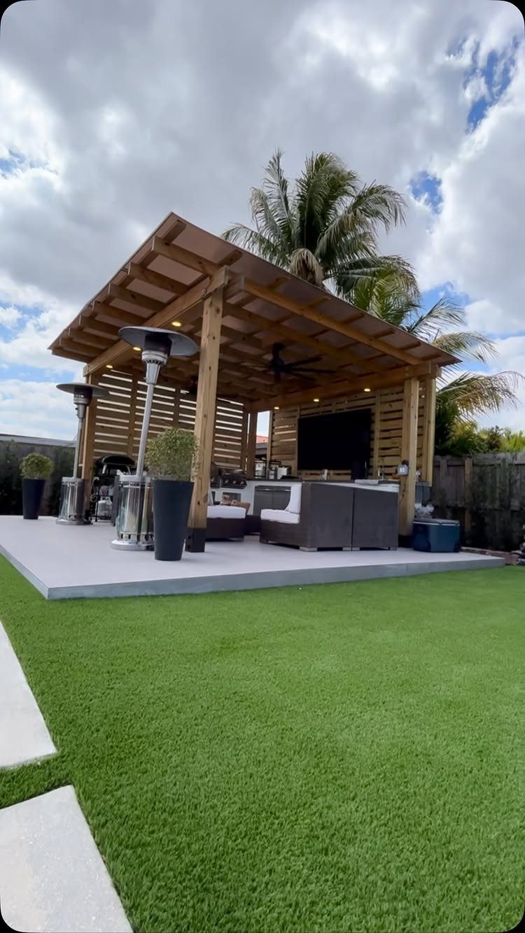A wooden pergola covering a modern outdoor patio area with seating and heaters next to a lawn.
