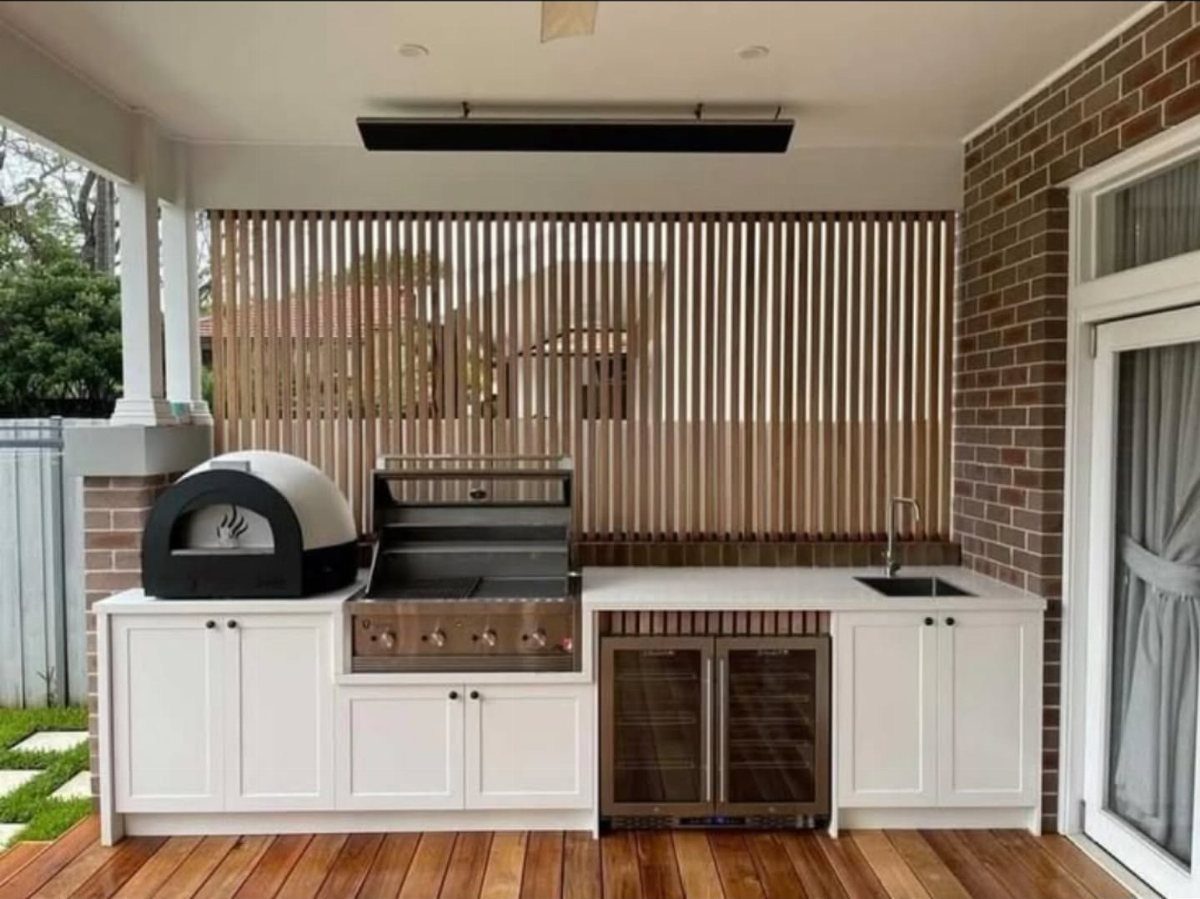 White outdoor kitchen cabinetry with a grill and pizza oven installed on a wooden deck.