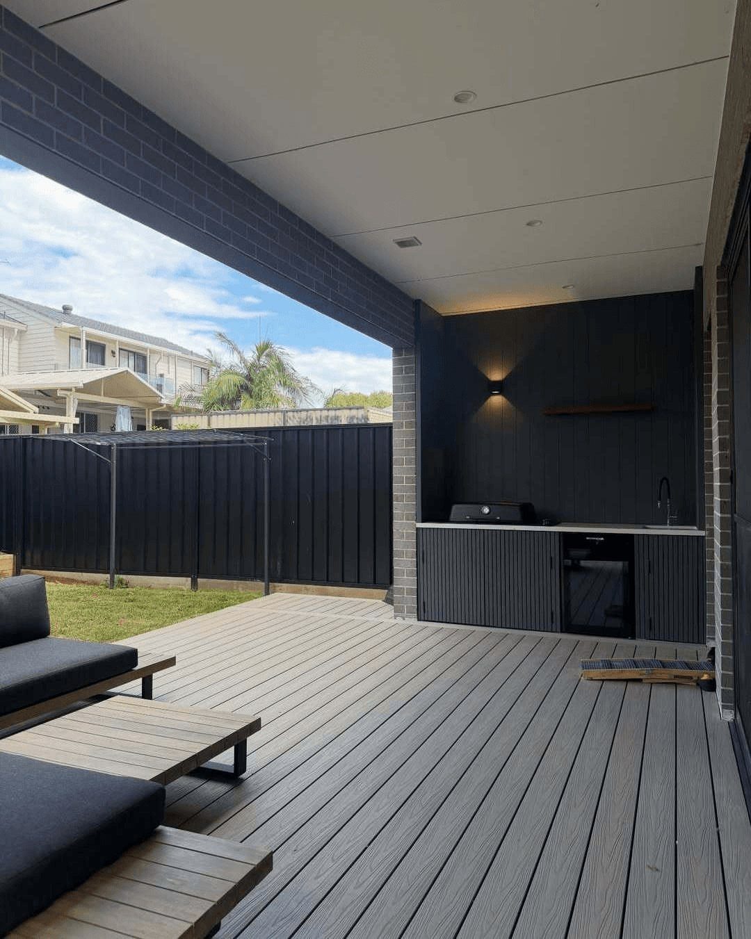 Grey composite decking boards leading to a modern dark outdoor kitchen under a covered patio.