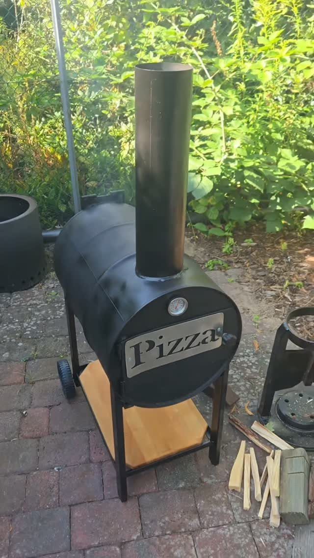 A black cylindrical metal pizza oven with a tall chimney on a brick patio.