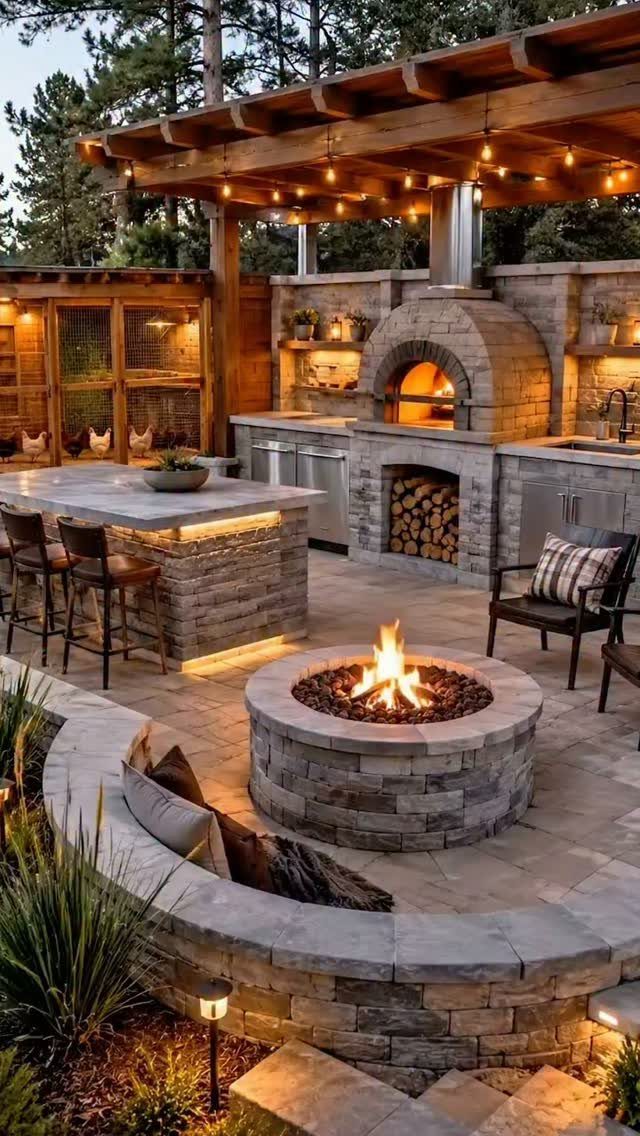 Stone outdoor kitchen with a wood-fired pizza oven and a circular fire pit on a patio.
