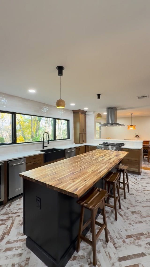 A large kitchen island featuring a thick butcher block wooden countertop and dark base with wooden stools.