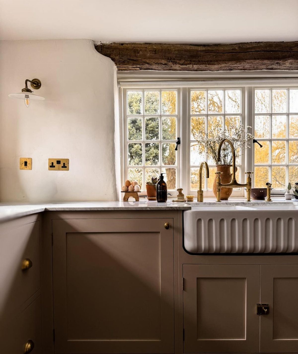 Taupe Shaker-style cabinets and a white farmhouse sink in a rustic kitchen setting.