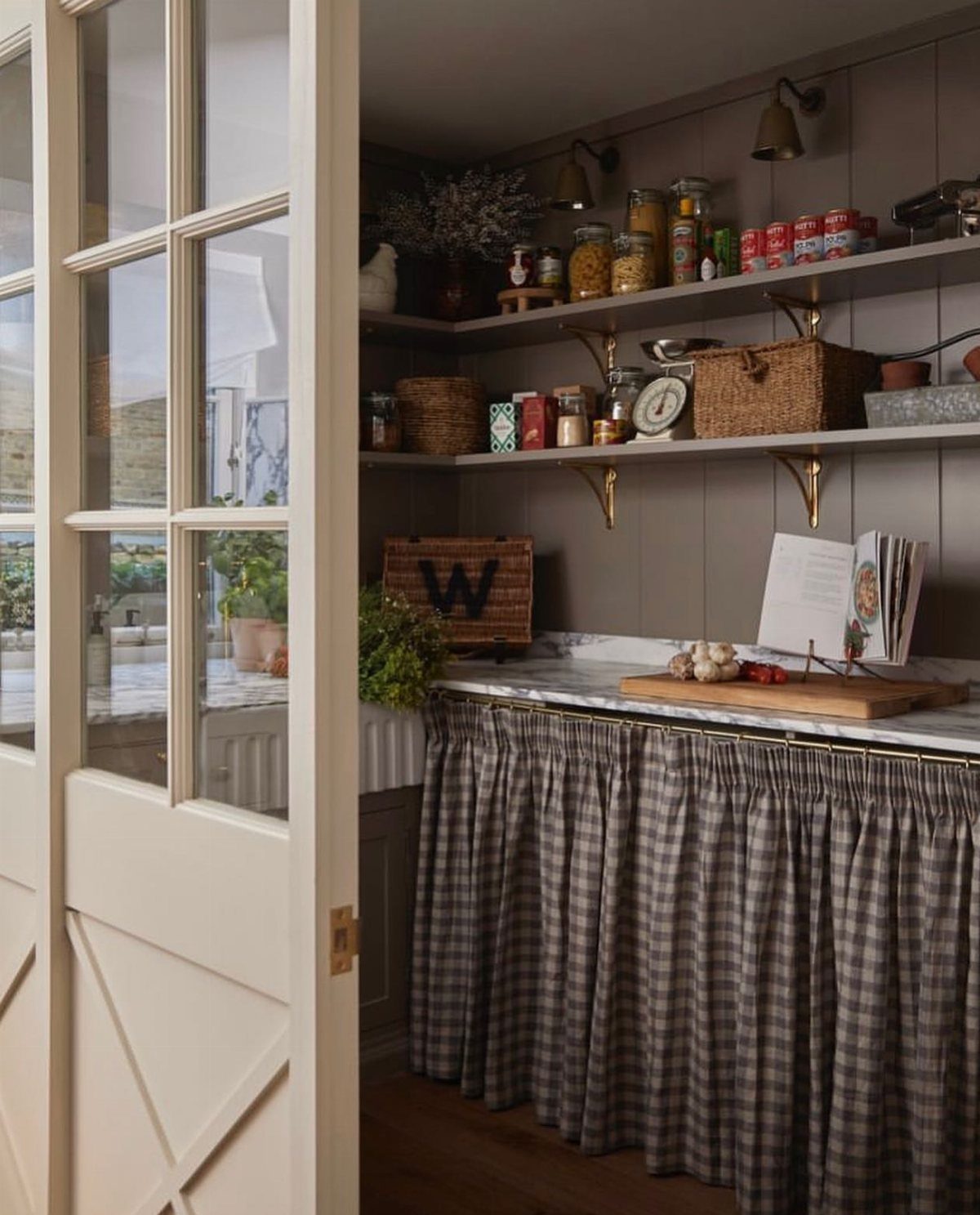 Grey checkered fabric skirt covering kitchen cabinets under a marble countertop and open shelving.