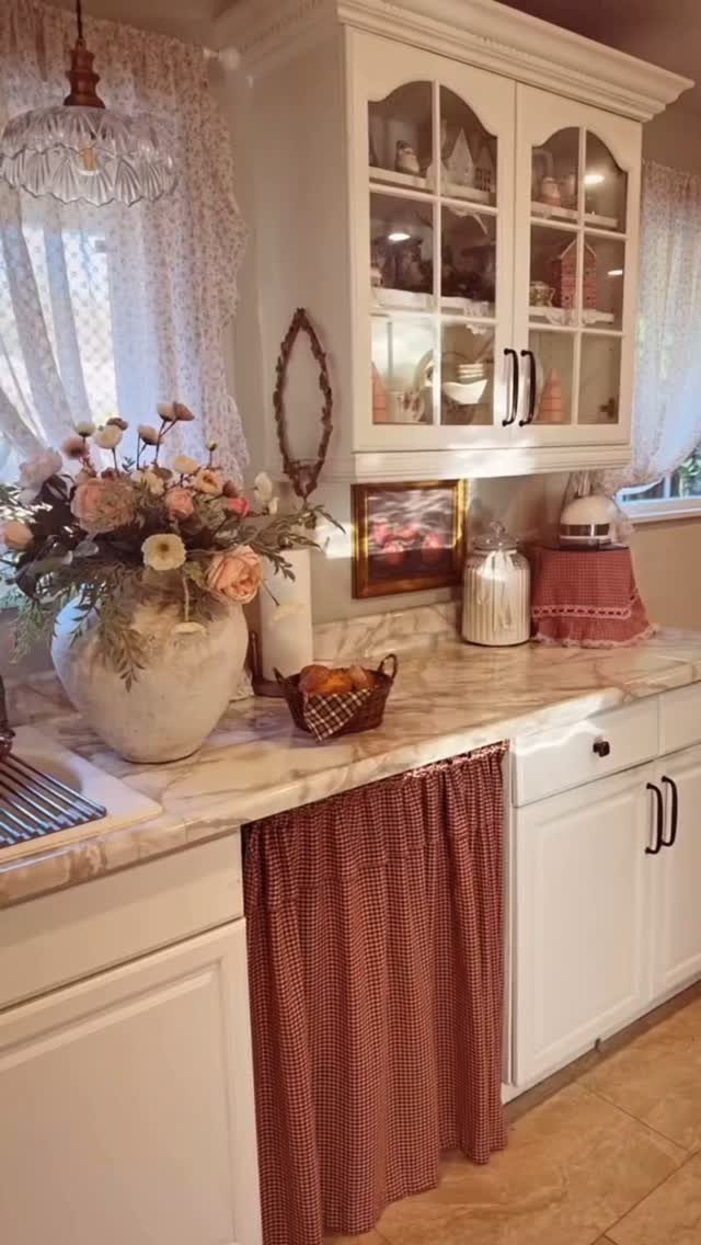 A rustic kitchen counter with marble tops, white cabinets, and vintage decor items including flowers and ceramic vases.