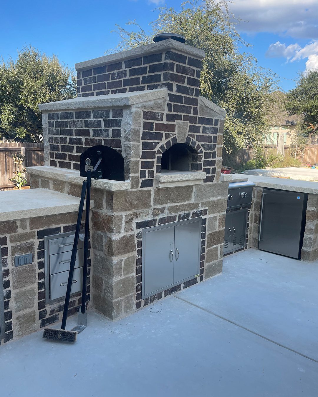 A brick and stone outdoor kitchen with built-in ovens and stainless steel storage cabinets.
