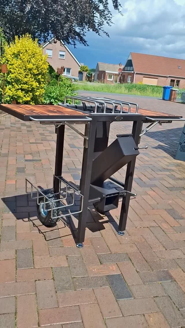 A black metal rocket stove cooking station on a brick patio outdoors.