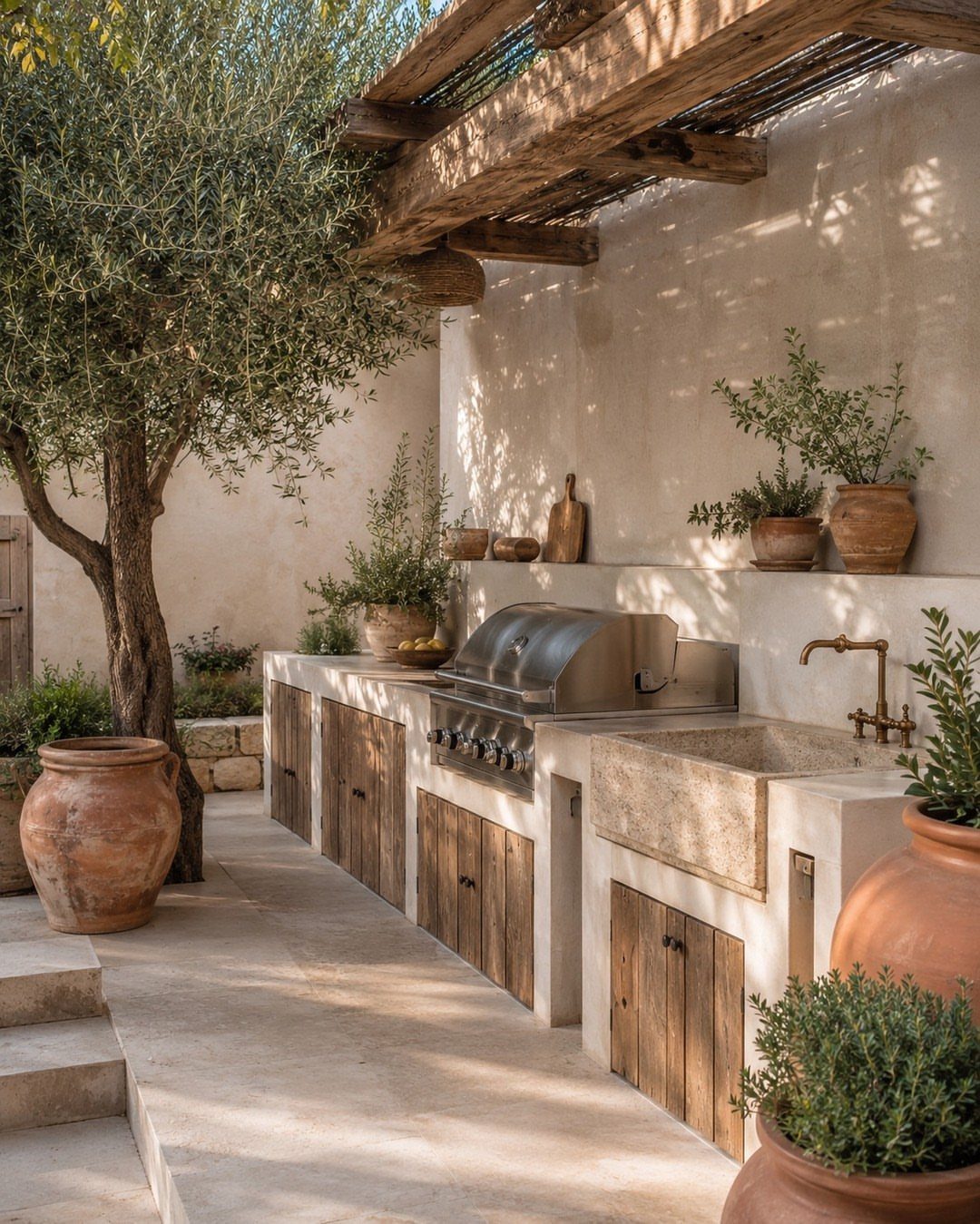 A rustic outdoor kitchen with a stainless steel grill, stone sink, and wooden cabinets in a courtyard.