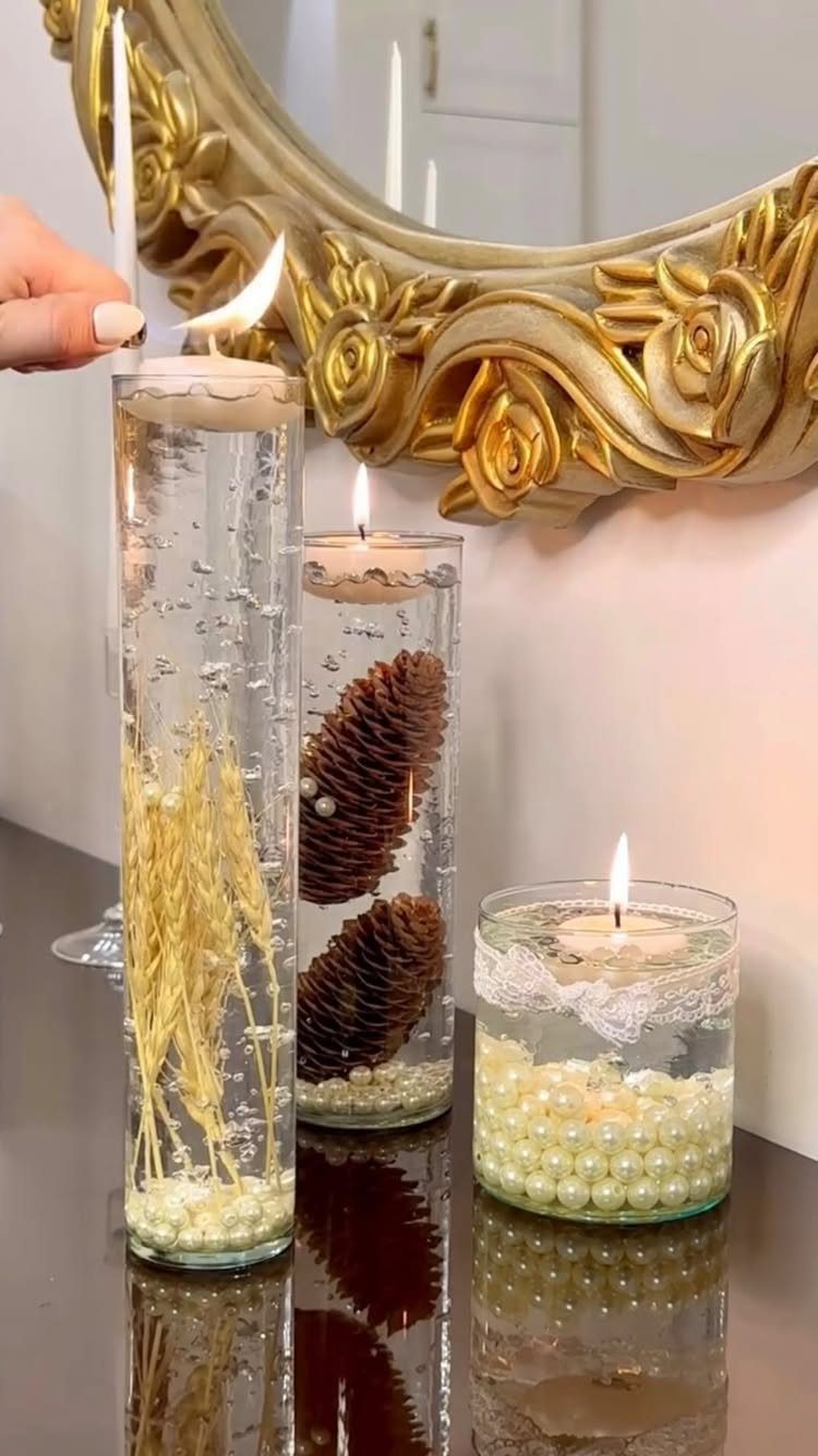 Three glass cylinder candle holders with floating candles and decorative elements on a reflective surface.