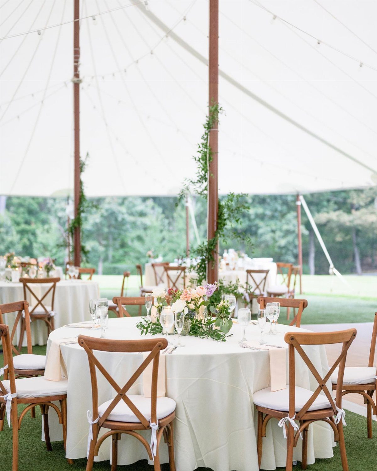 A round table decorated with cream linens, glassware, and a floral centerpiece under a white tent.