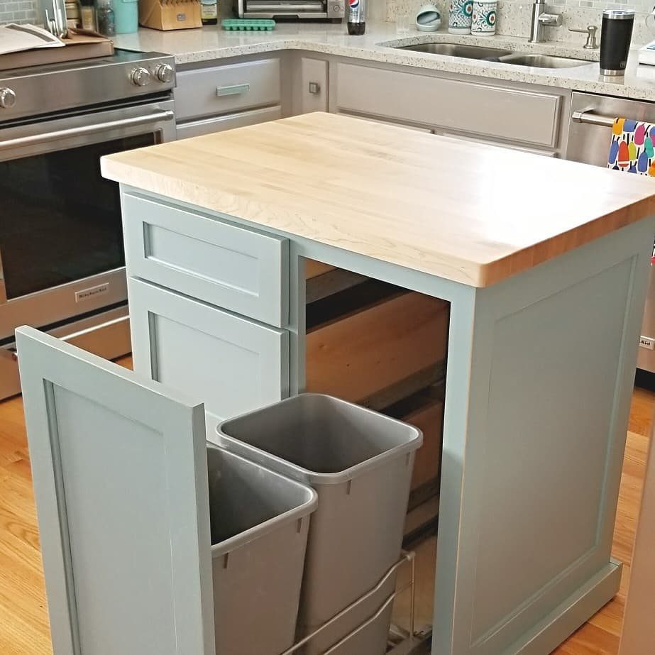 A light blue kitchen island with a wooden countertop and grey trash bins in an open drawer.