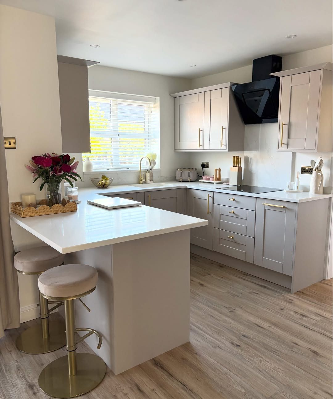 A modern kitchen with light grey cabinets and a white peninsula island with two bar stools.