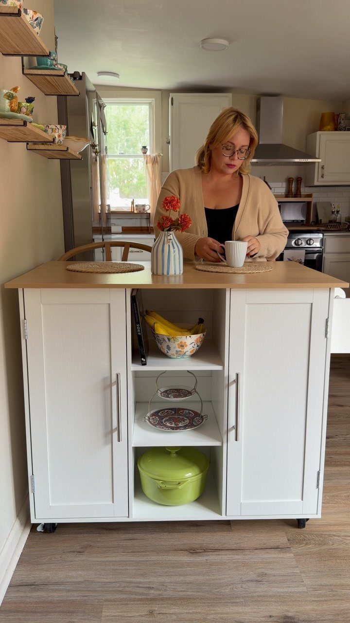 A white mobile kitchen island with a wooden top and open shelving on wheels.