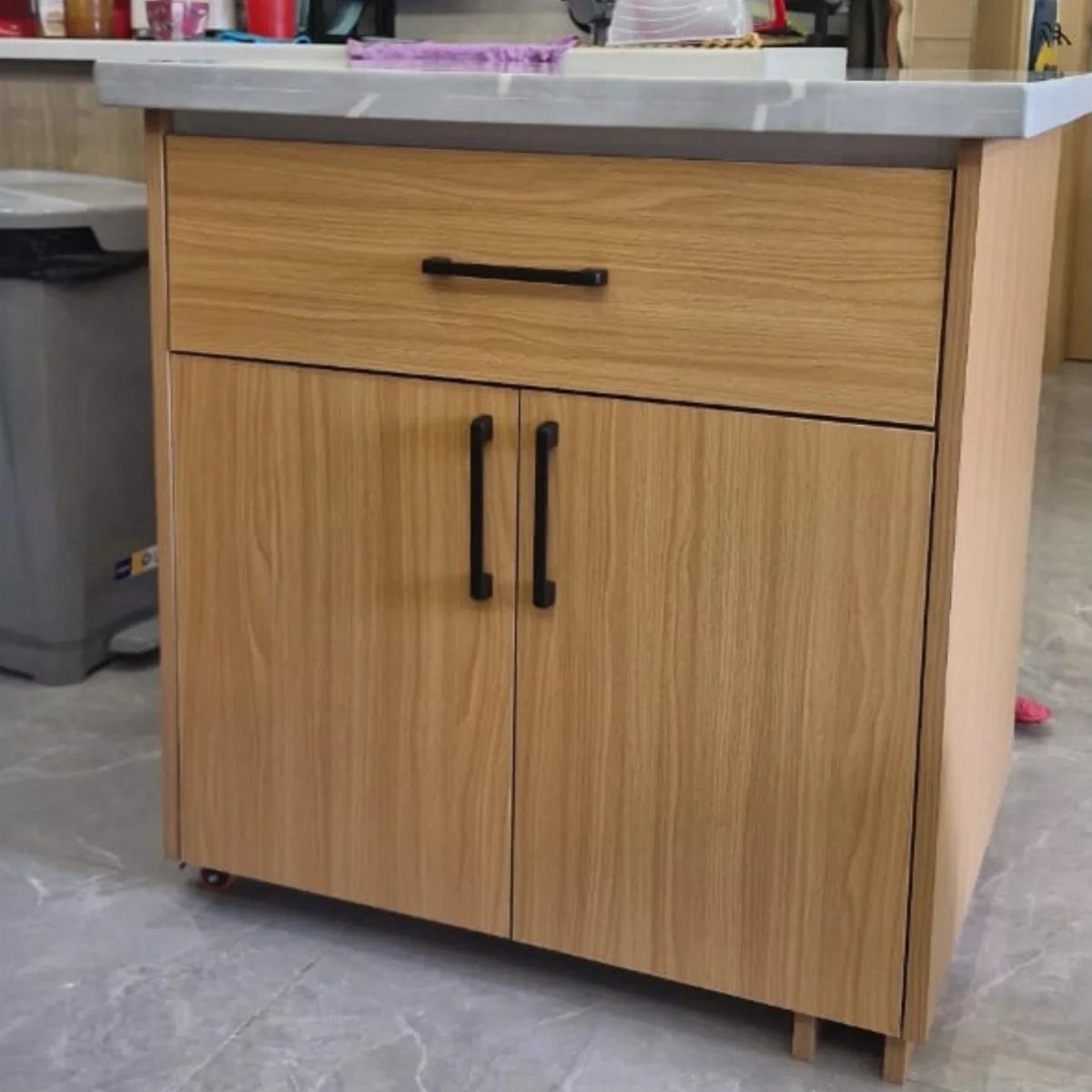 A light wood kitchen island with a white countertop and black handles on a tiled floor.