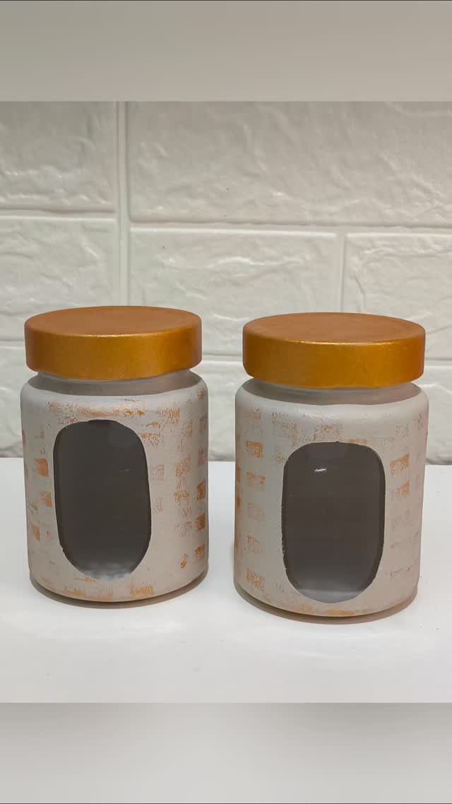 Two small glass jars with gold lids and white brick patterns on a white surface.