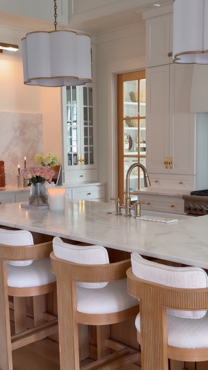 White marble kitchen island with grey veining, white cabinetry, and light wood barstools.