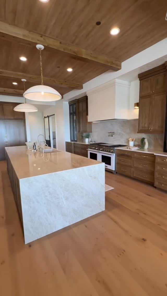 A spacious kitchen featuring a large marble island and a warm wood planked ceiling with beams.