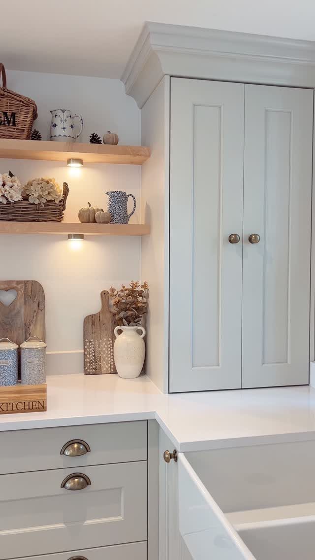 White kitchen cabinets with vintage brass hardware and open wooden shelves holding decorative pottery.
